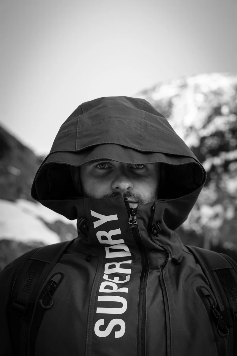Lukáš Granatier v bundě s kapucí, za ním zasněžený horský svah