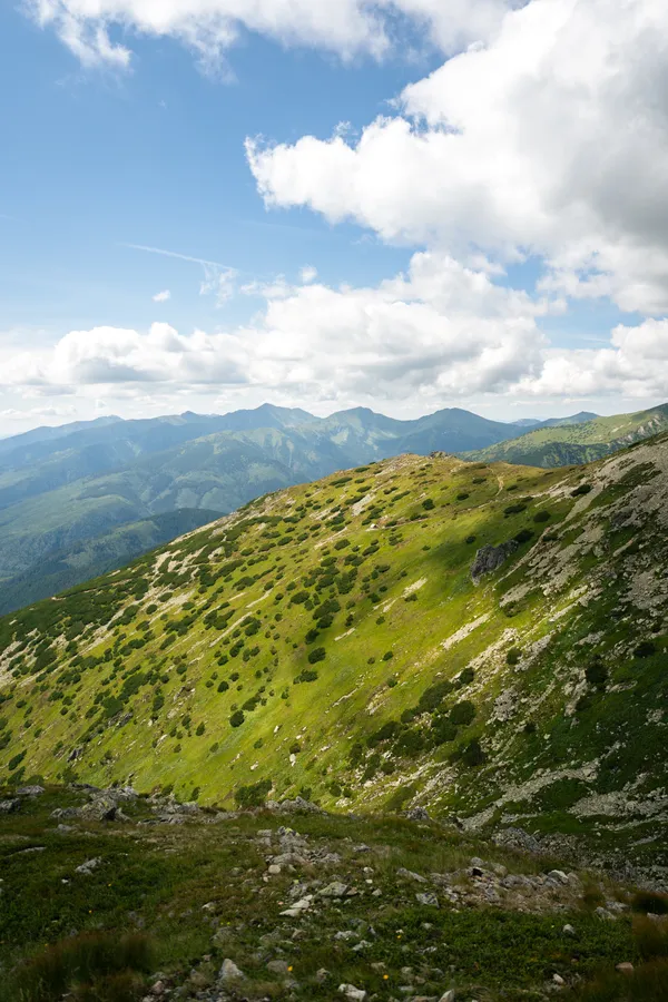 Zelené horské svahy a vzdálené hřebeny pod oblohou s mraky