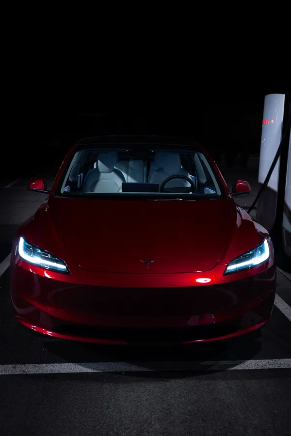 Červený automobil s rozsvícenými světlomety u nabíjecího stojanu v noci